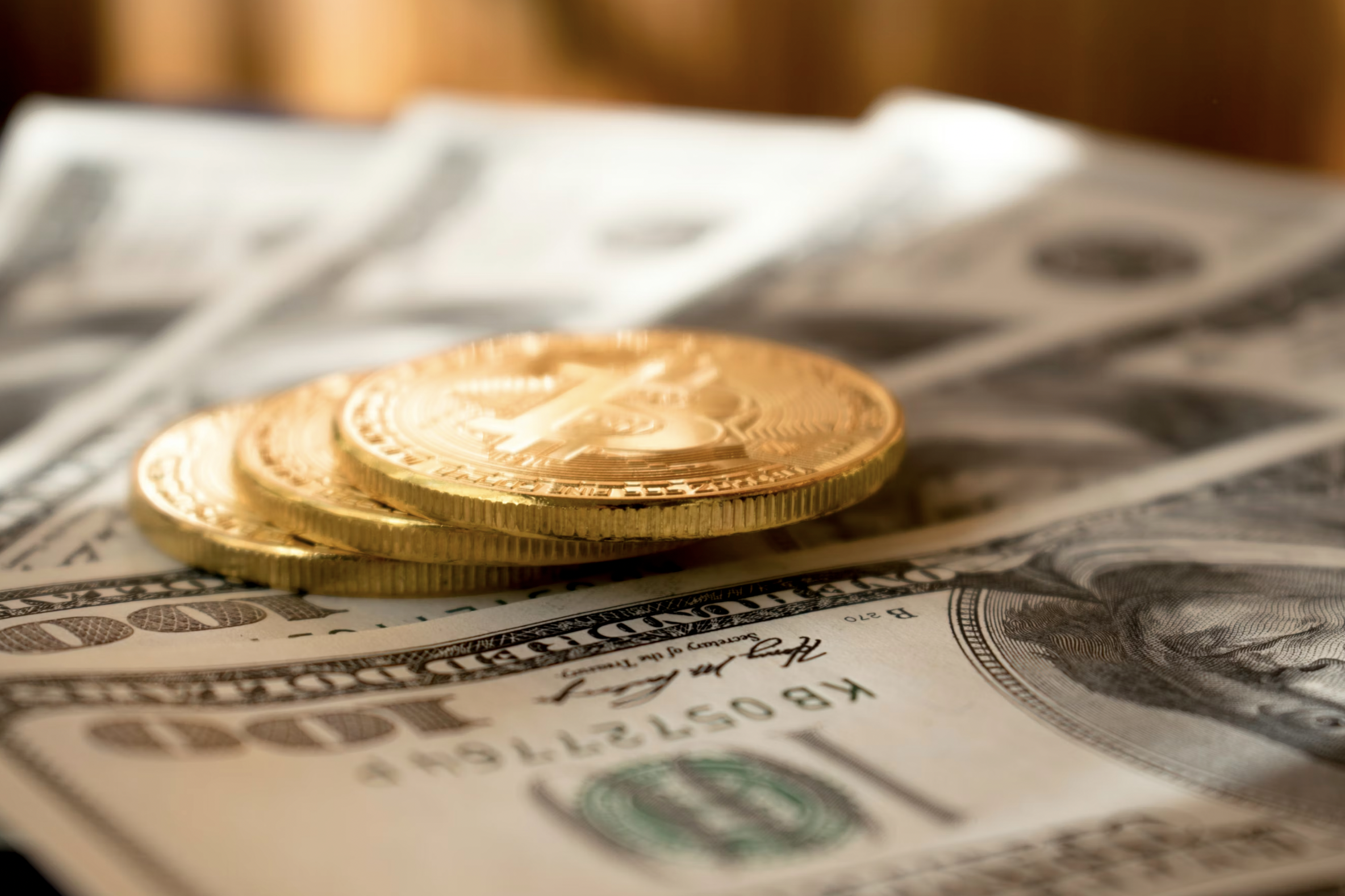 Close-up of stacked gold coins resting on scattered U.S. dollar bills, focusing on coin details