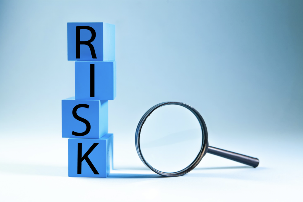 Stack of blue blocks spelling RISK with a magnifying glass beside them, symbolizing risk investigation or analysis.