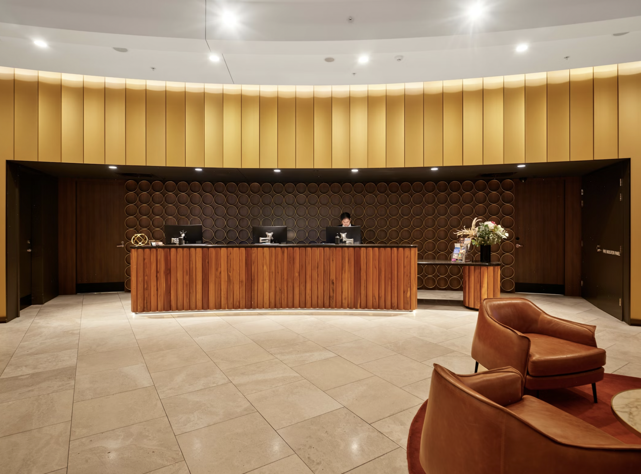 Hotel reception desk in a warm lobby with vertical wood panels and circular wall design behind the counter.