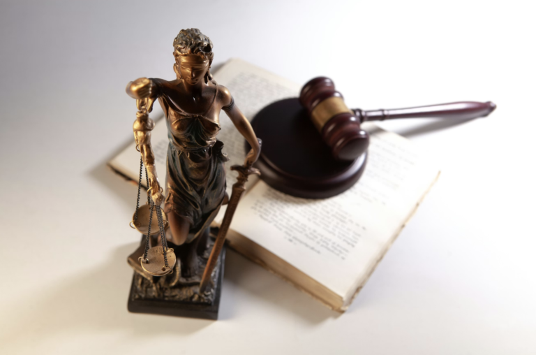 Statue of Lady Justice holding scales with a gavel and open law book in the background