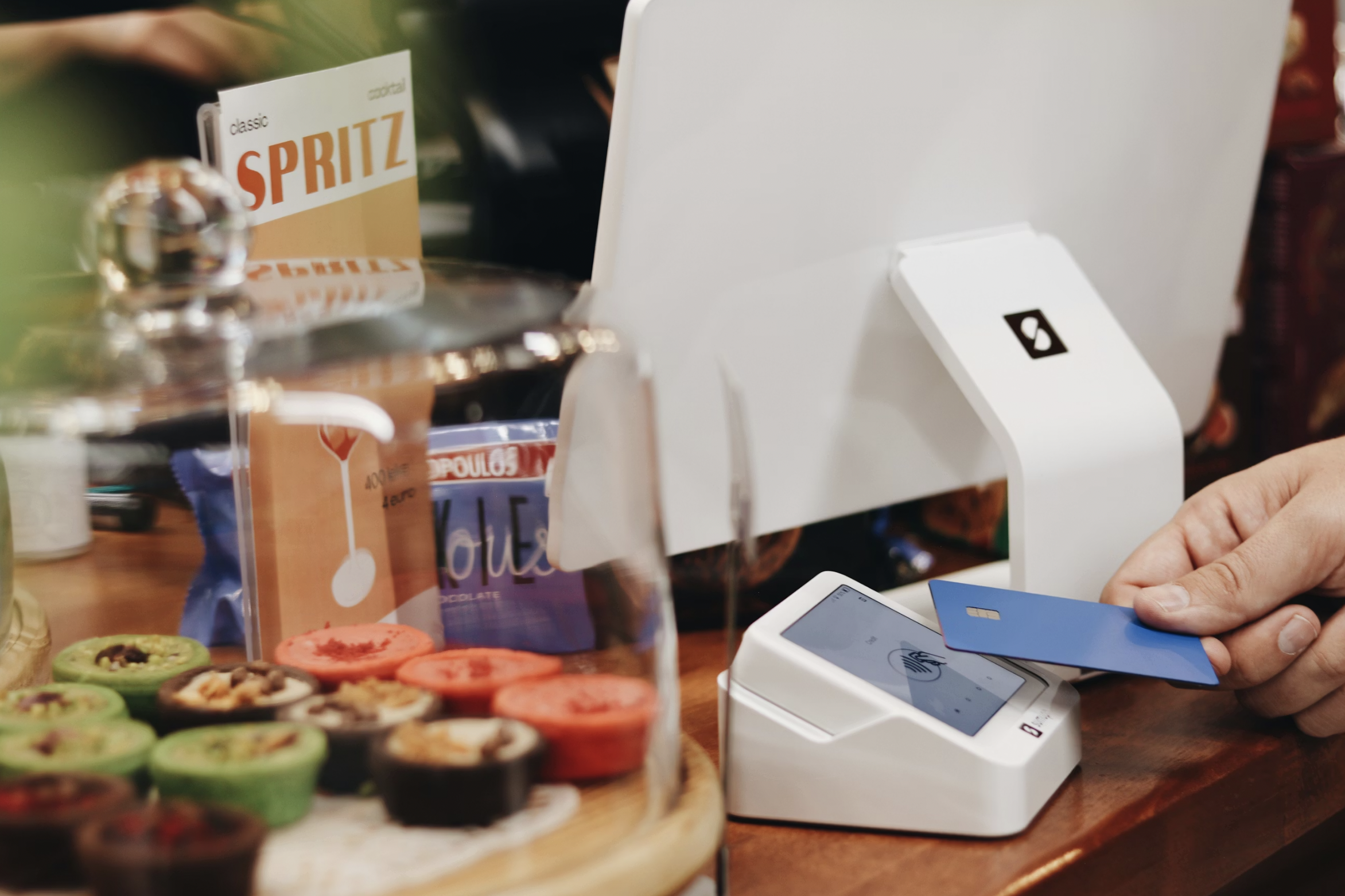 Person using a card payment terminal at a cafe counter, with colorful donuts in the foreground.