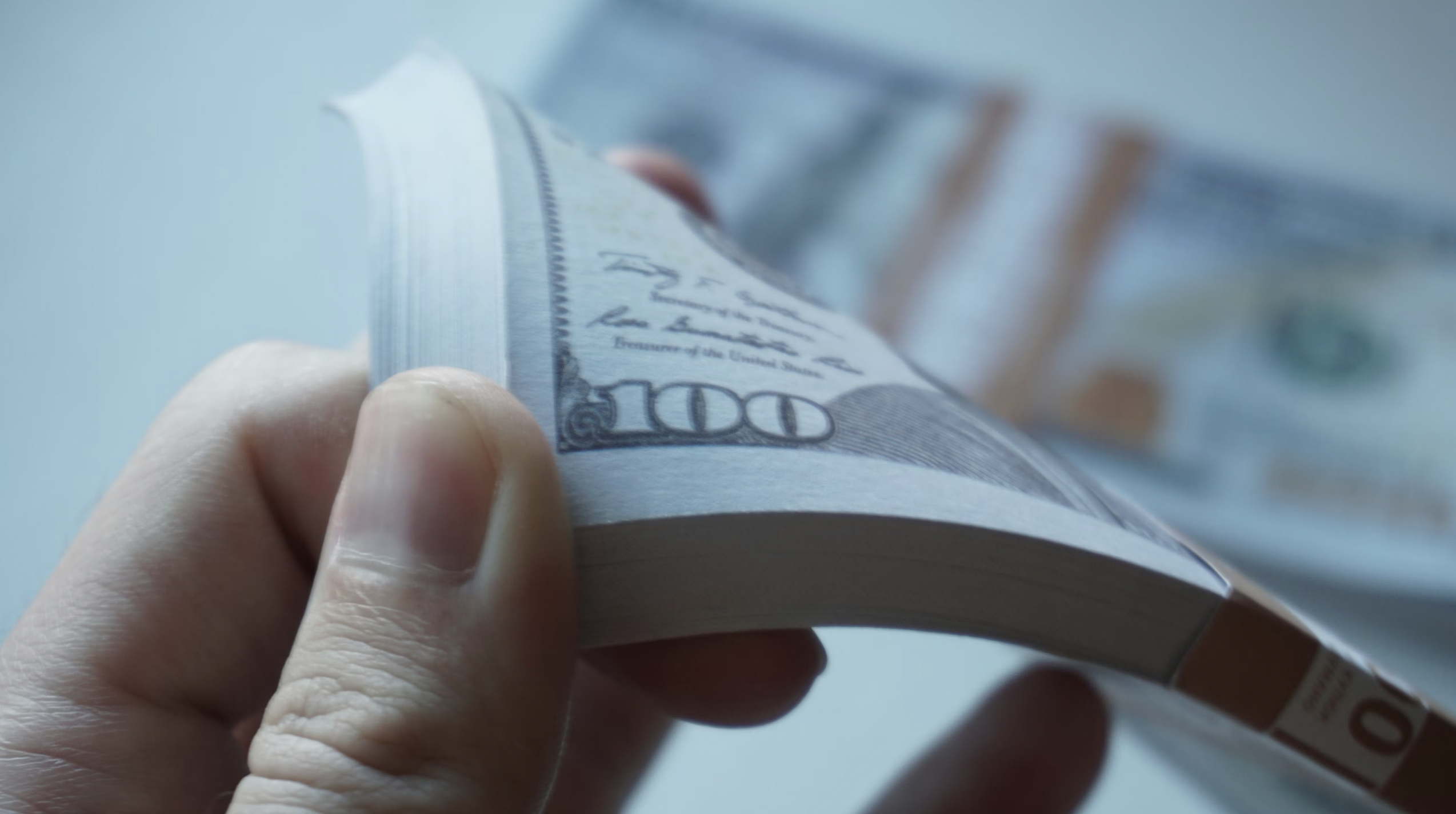 Close-up of a hand folding a US $100 bill while counting money, with the number 100 visible on the note era.