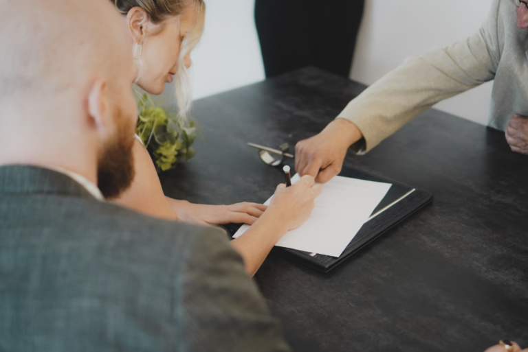 People seated around a dark table while signing a document, with one person writing on a white sheet.