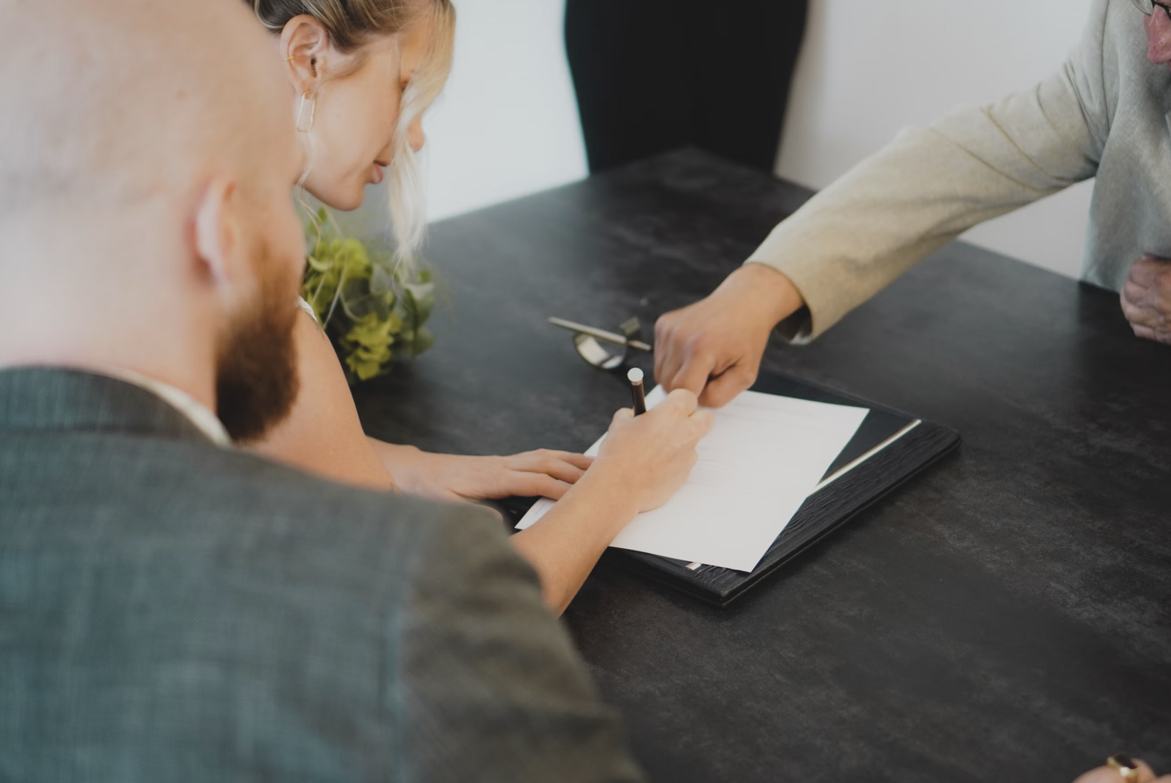 People seated around a dark table while signing a document, with one person writing on a white sheet.