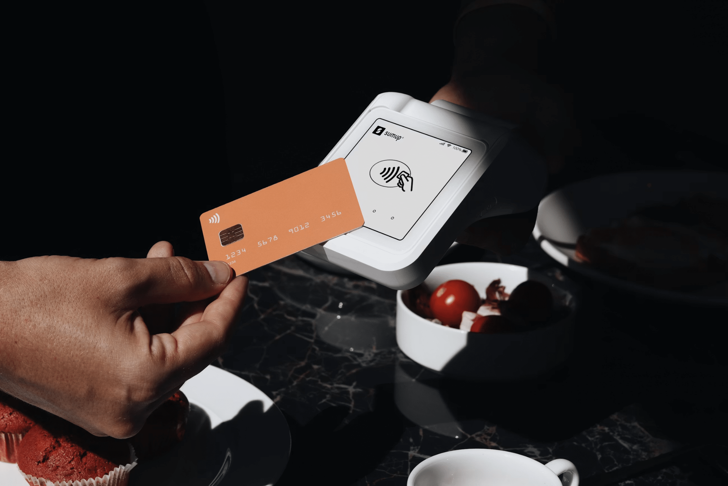 Close-up of a hand tapping an orange contactless card on a white payment terminal