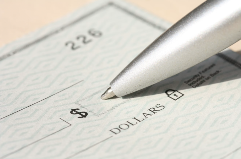 Close-up of a silver pen resting on a blank check, with dollar amount fields and printed text visible