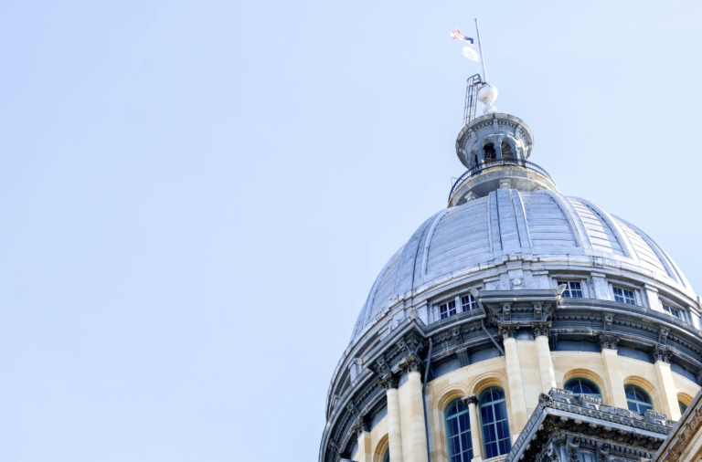 Close-up of a domed, neoclassical building with a flag on top against a blue sky.