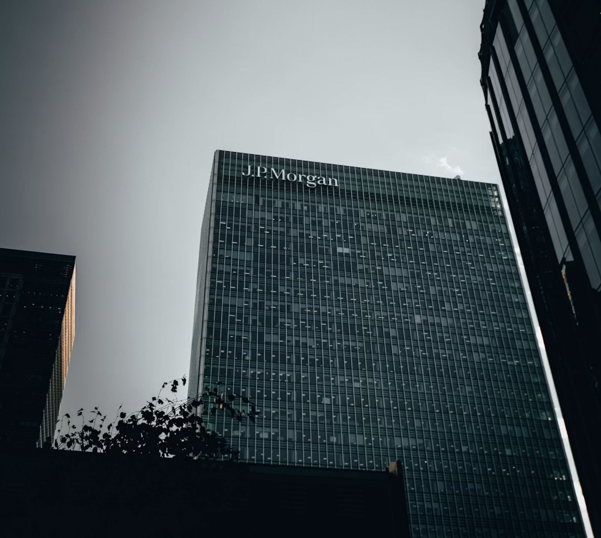Tall modern office building with J.P. Morgan signage seen from below against a gray sky.