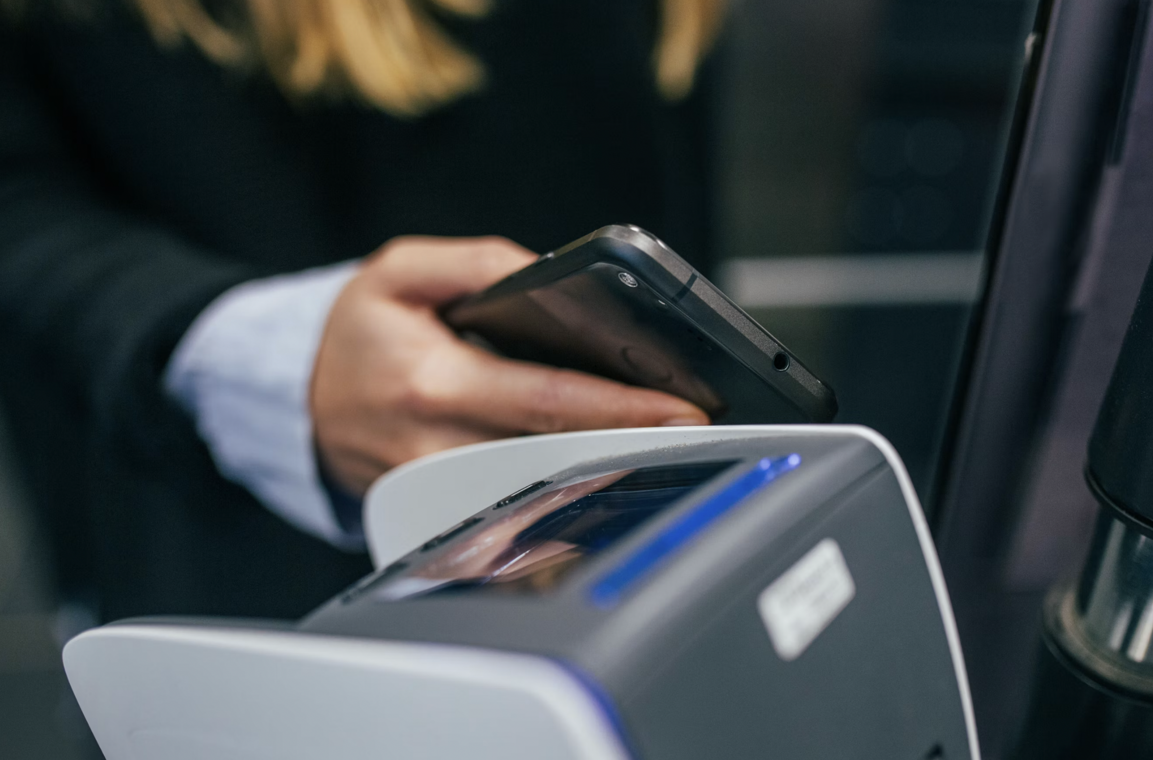 Person holding a smartphone near a payment terminal, ready to make a contactless payment at checkout