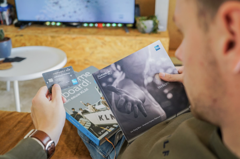 Person holding travel brochures and a card near a wooden table, with a blurred TV in the background.