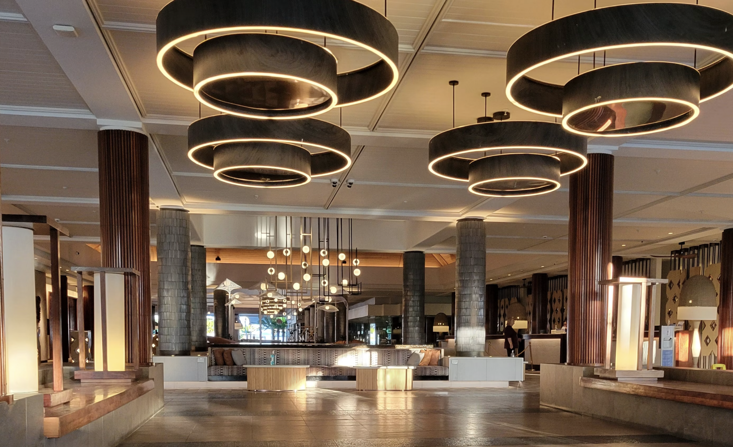 Interior showroom with large circular halo pendant lights hanging from the ceiling and wood columns in the foreground.